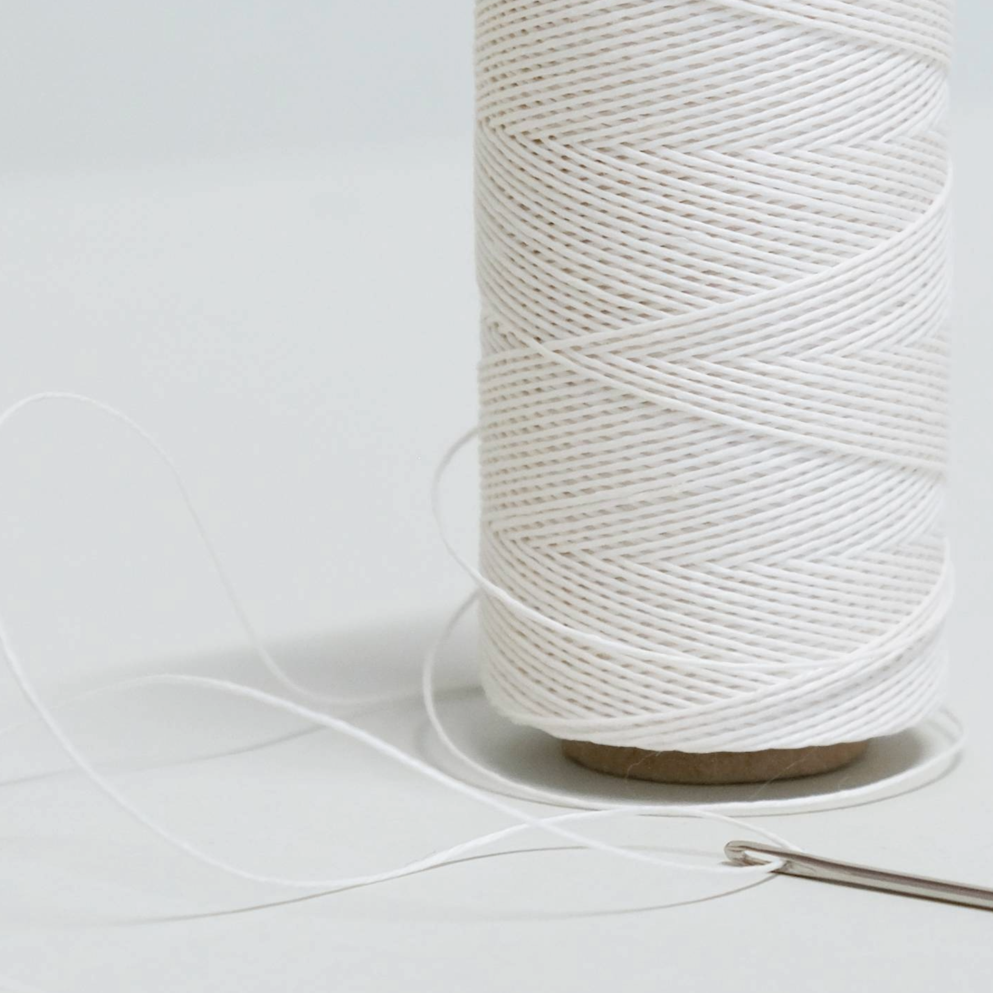 Close up of a spool of white thread on a light grey background