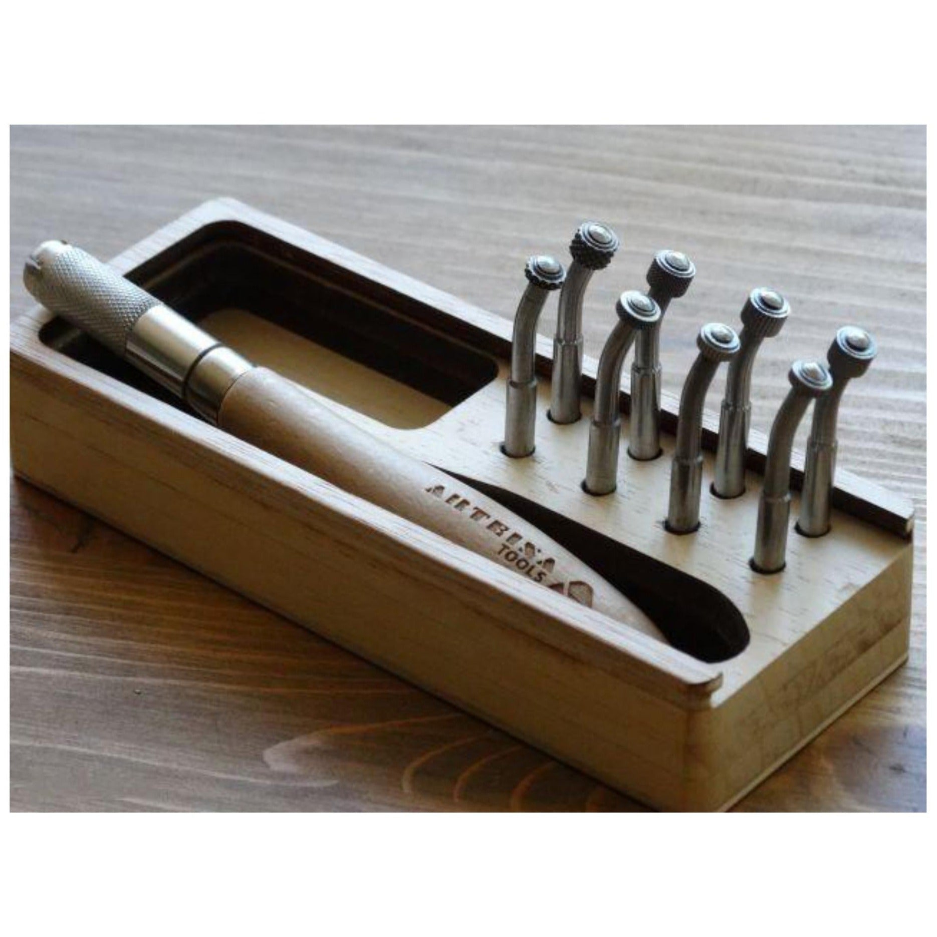 A set of Arteina interchangeable roulette heads displayed in a wooden box with an ergonomic handle displayed on a wooden surface