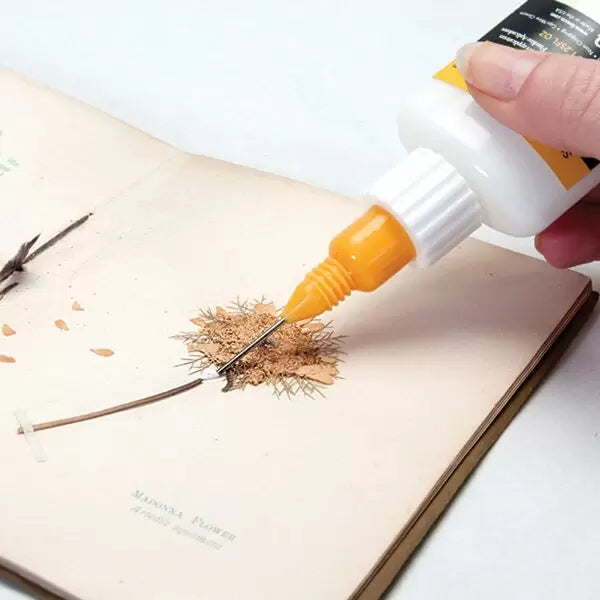 Lineco Fine Line Applicator filled with adhesive being used to adhere a specimen into a book.
