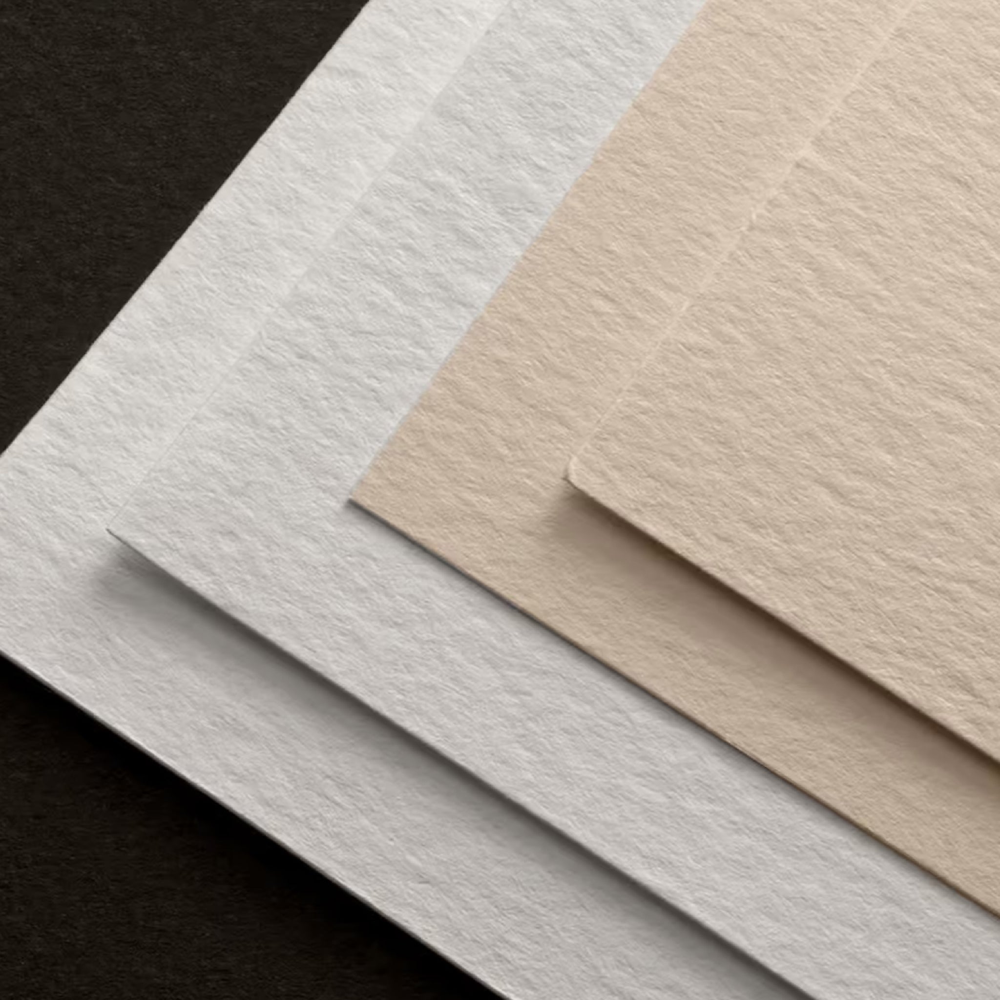 Close up of Fabriano Unica Papers in white and cream tones with straight edges and a light texture, displayed on a black background