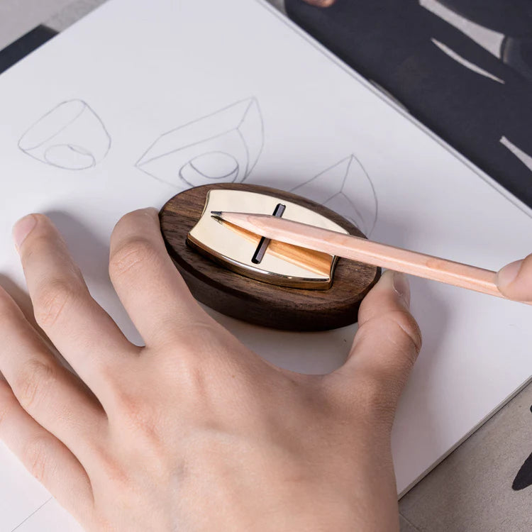 A Hovel Pencil Plane sitting in a wooden base held still while a a pencil is being sharpened. Set against a paper with technical drawings on it.