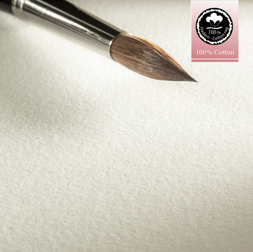 A close-up of a watercolour brush on Hahnemühle Expression Watercolour Paper, highlighting the paper's texture and tone with a 100% Cotton label.