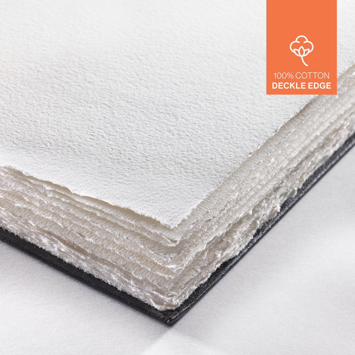 Close-up of a white paper sheets in a black hardcover book with deckle edges, featuring an orange 100% cotton label on the top right corner.