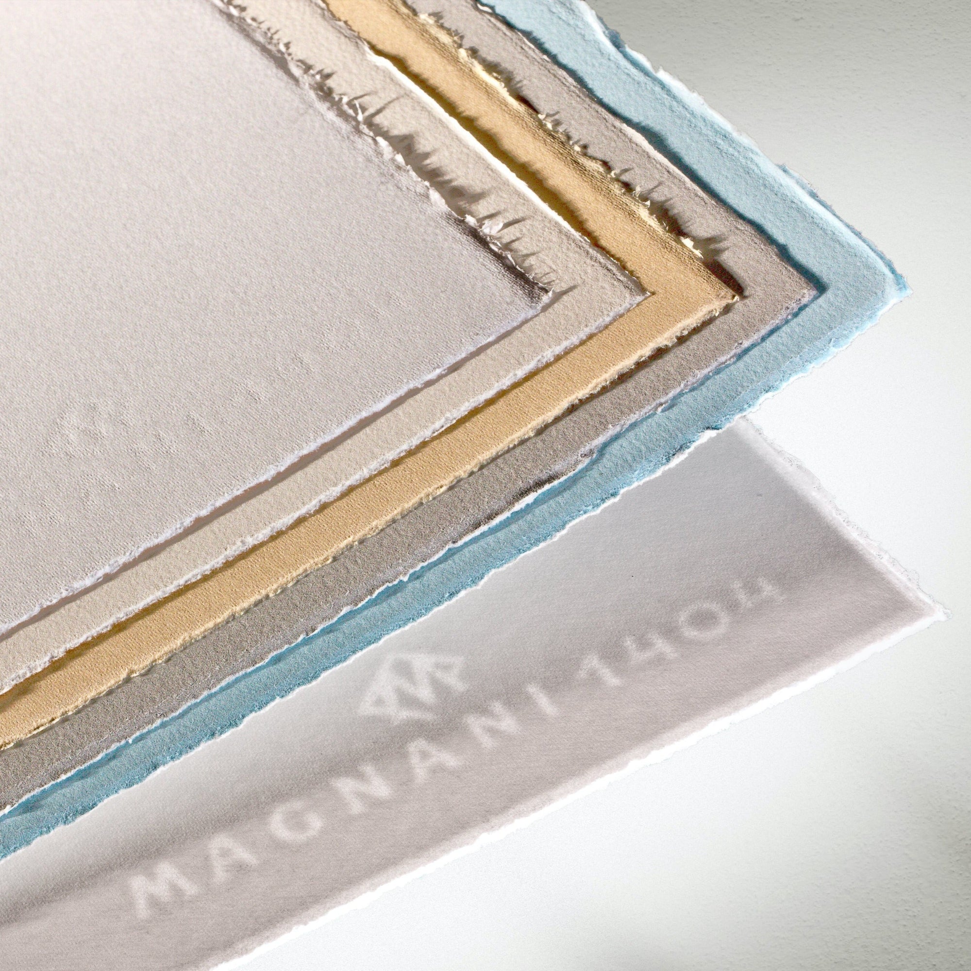 A selection of various coloured papers from the Magnani 1404 Pescia collection, showcasing a smooth texture and a watermark clearly visible on one of the sheets.