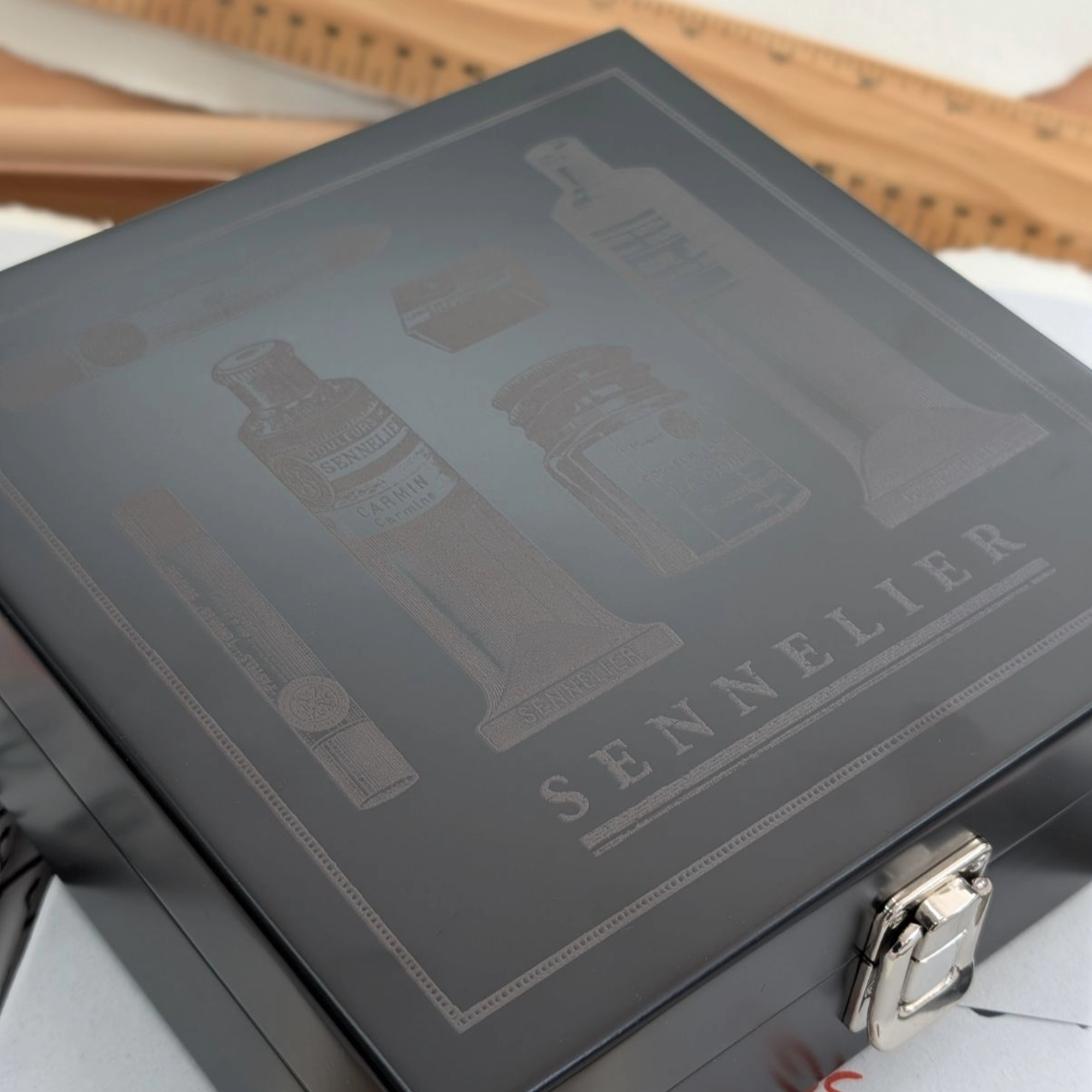 Sennelier art supply box with engraving illustrations on a black coated wooden surface