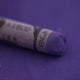 A close-up of a Sennelier large extra soft pastel on a purple background.