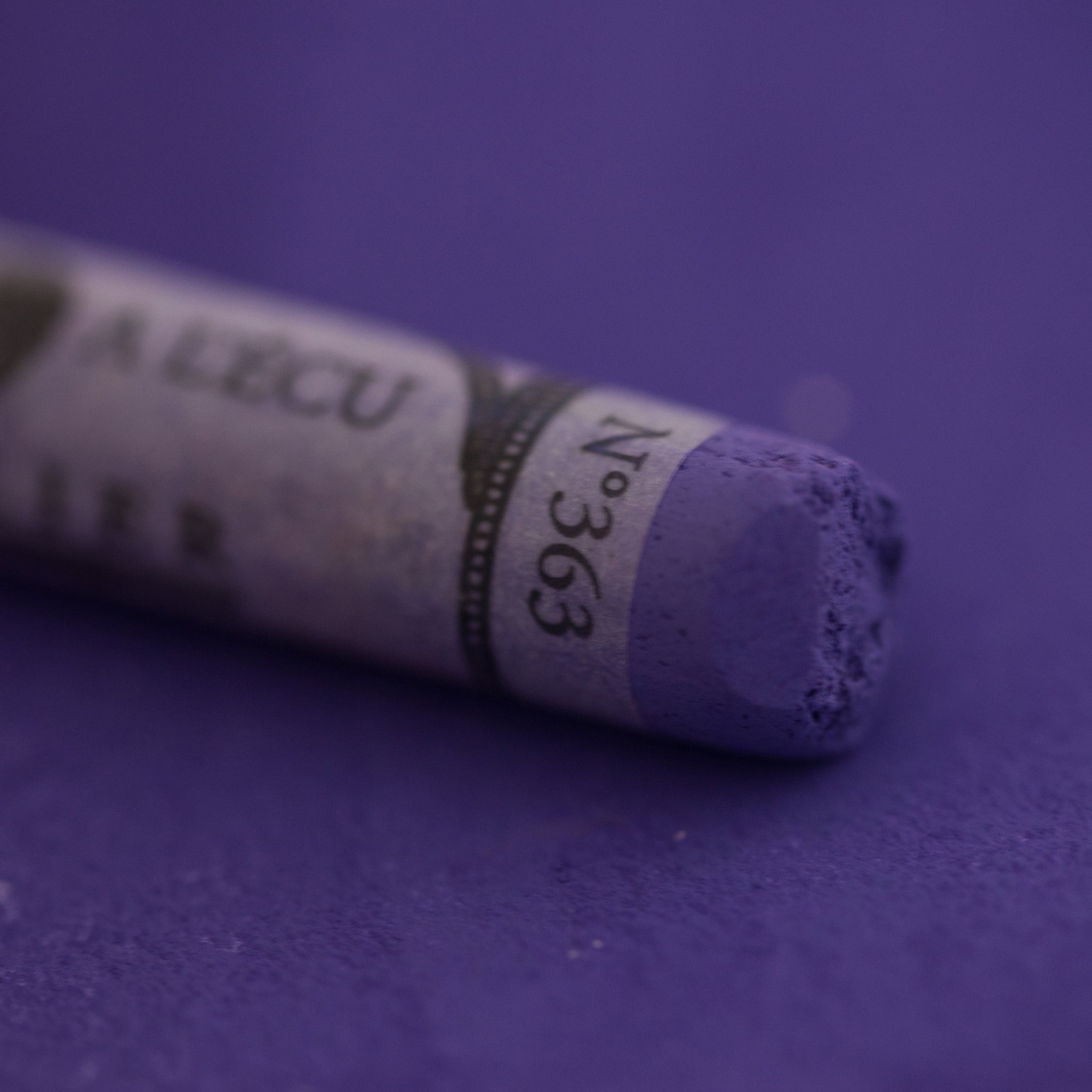 A close-up of a Sennelier large extra soft pastel on a purple background.