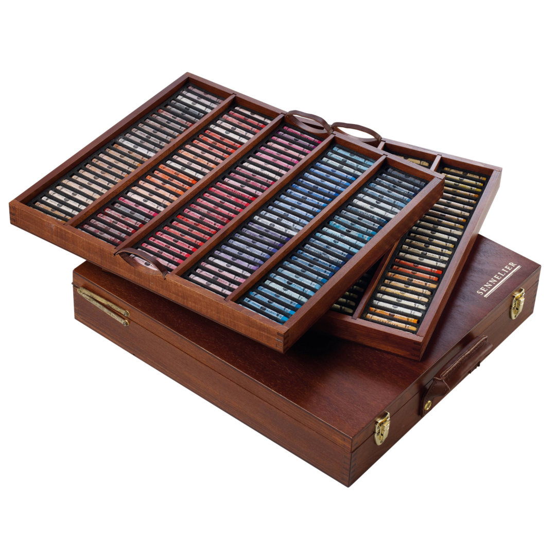 2 wooden trays of pastels of varying colours displayed atop a wooden box with leather handle on a white background.