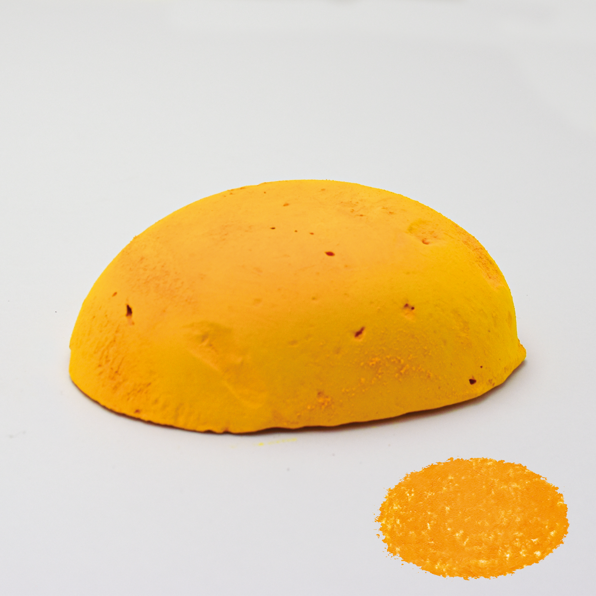 A half egg shaped pastel in a yellow tone, sitting on a white background with a drawn colour swatch.