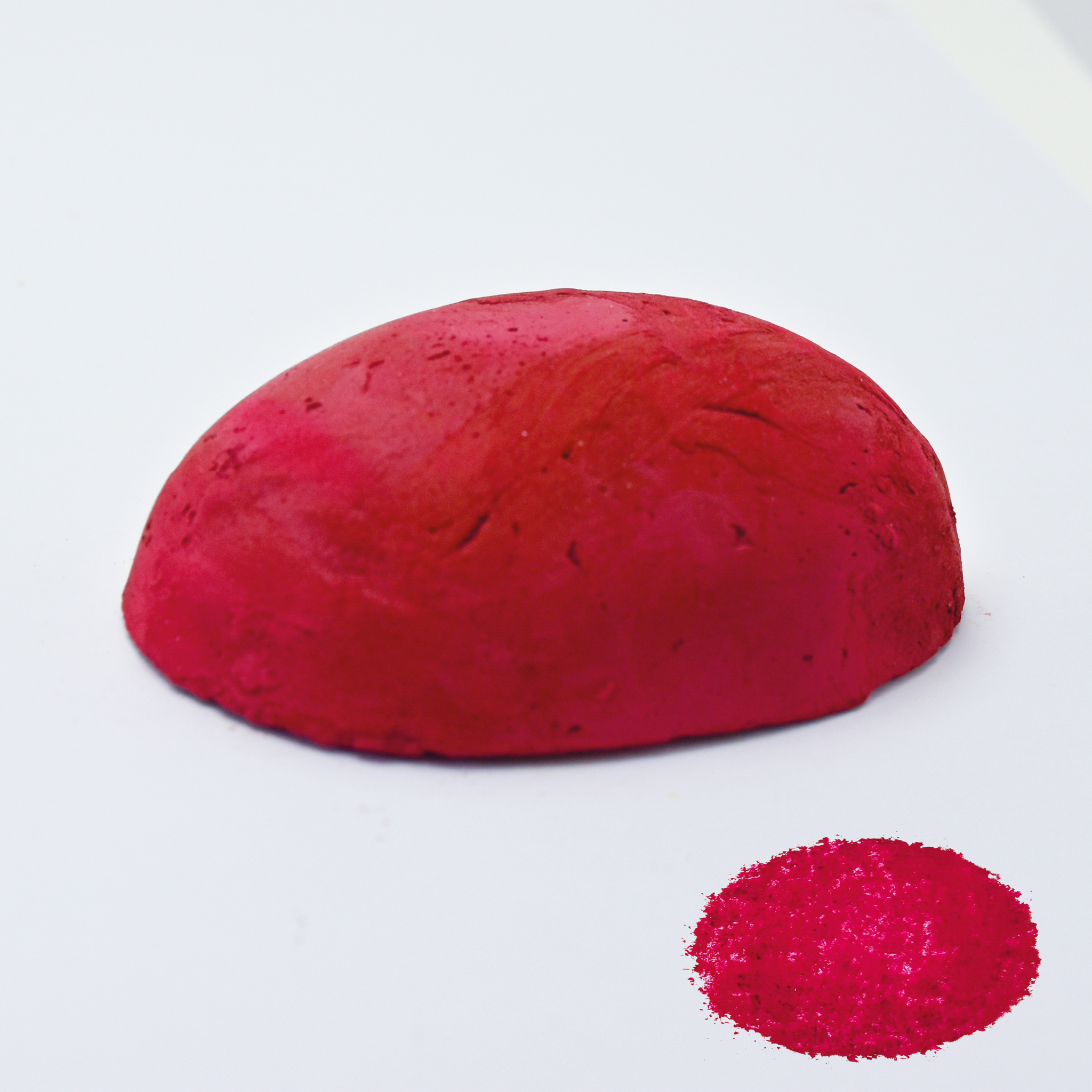 A half egg shaped pastel in a cool red tone, sitting on a white background with a drawn colour swatch.