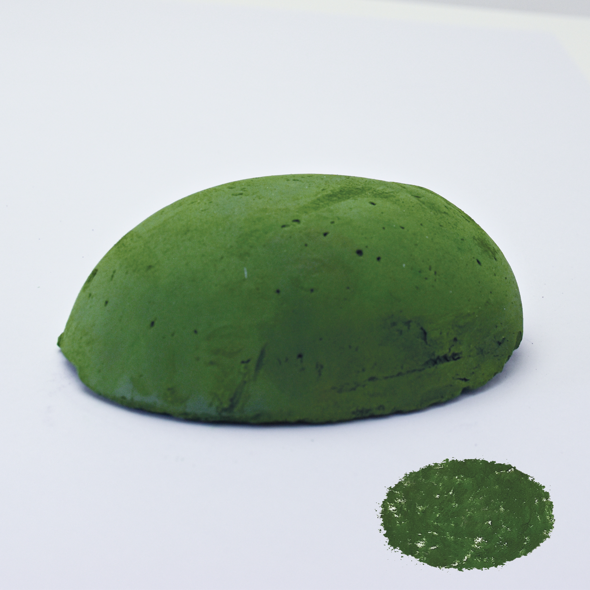 A half egg shaped pastel in a green tone, sitting on a white background with a drawn colour swatch.