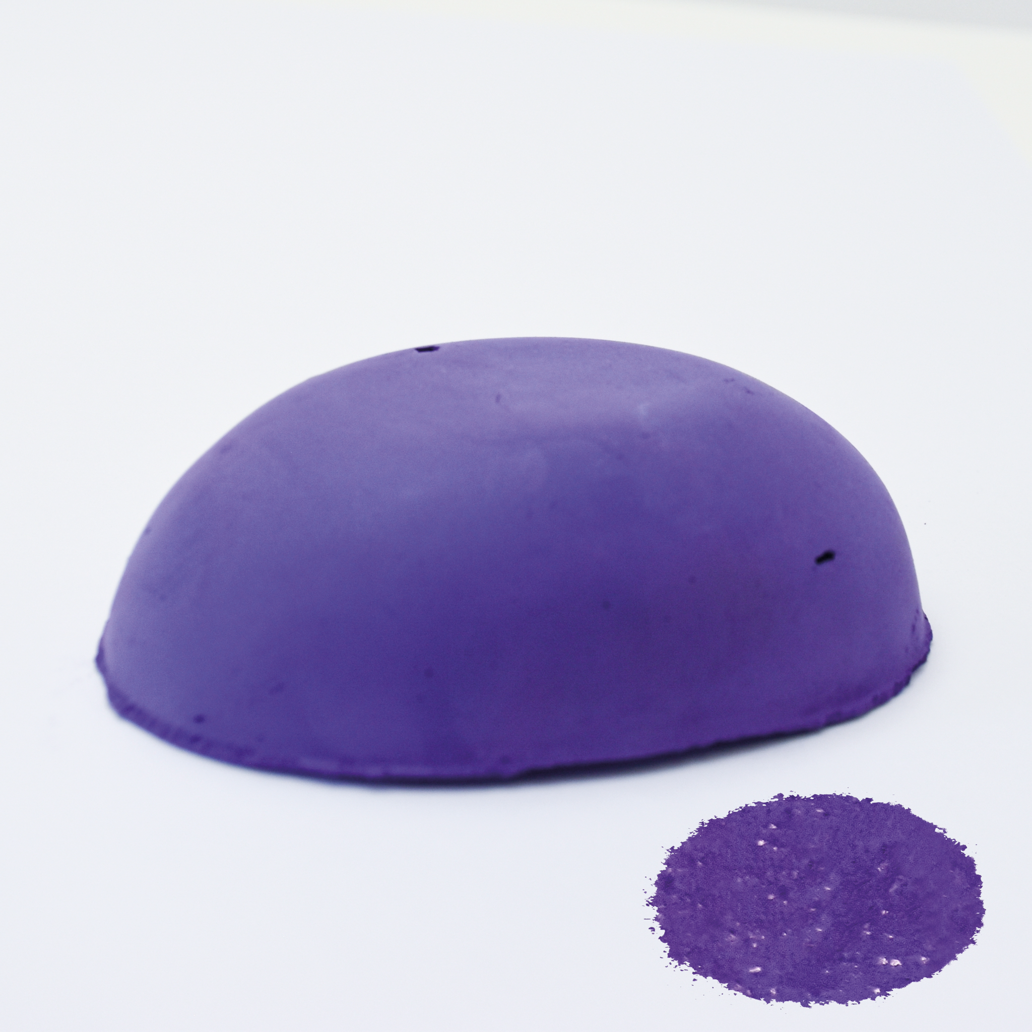 A half egg shaped pastel in a purple tone, sitting on a white background with a drawn colour swatch.