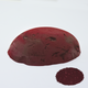 A half egg shaped pastel in a red brown tone, sitting on a white background with a drawn colour swatch.