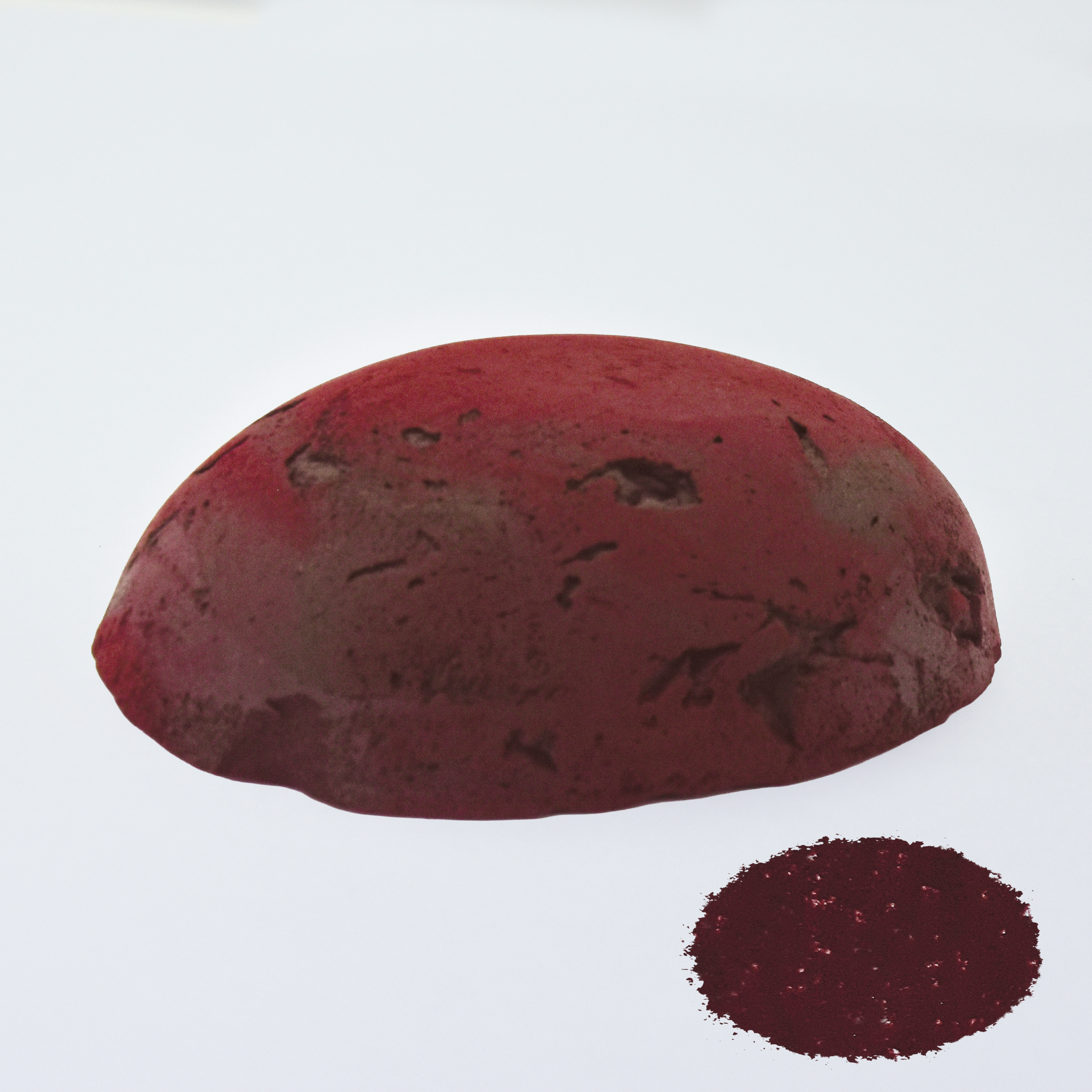 A half egg shaped pastel in a red brown tone, sitting on a white background with a drawn colour swatch.