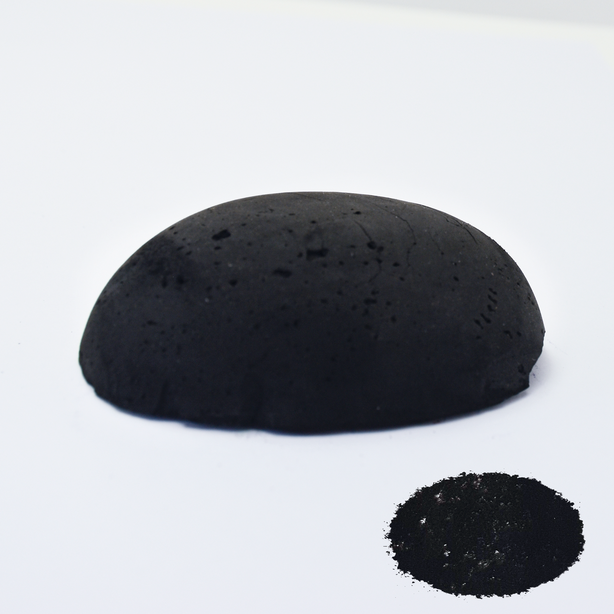 A half egg shaped pastel in black, sitting on a white background with a drawn colour swatch.