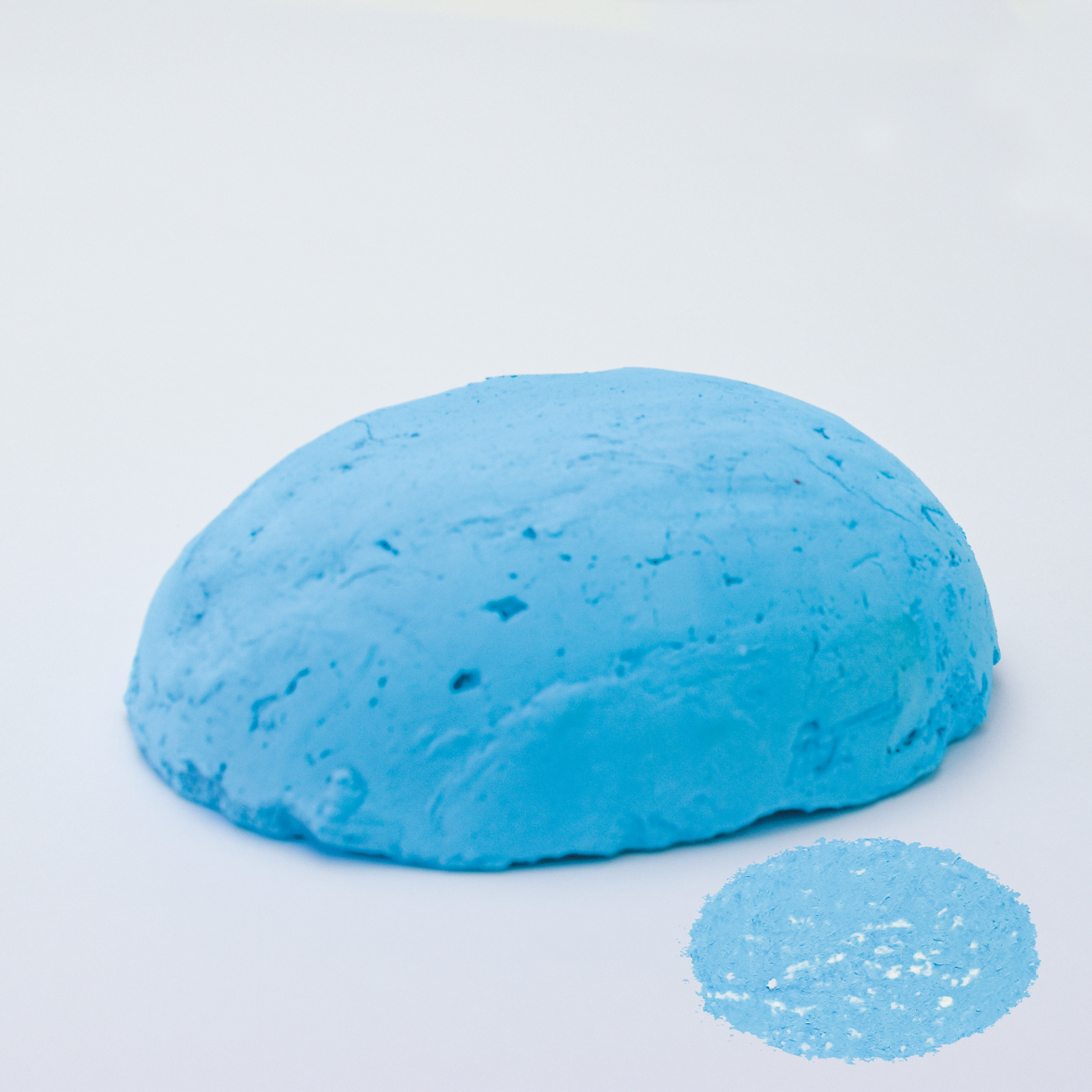 A half egg shaped pastel in a light blue tone, sitting on a white background with a drawn colour swatch.
