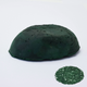 A half egg shaped pastel in a dark green tone, sitting on a white background with a drawn colour swatch.