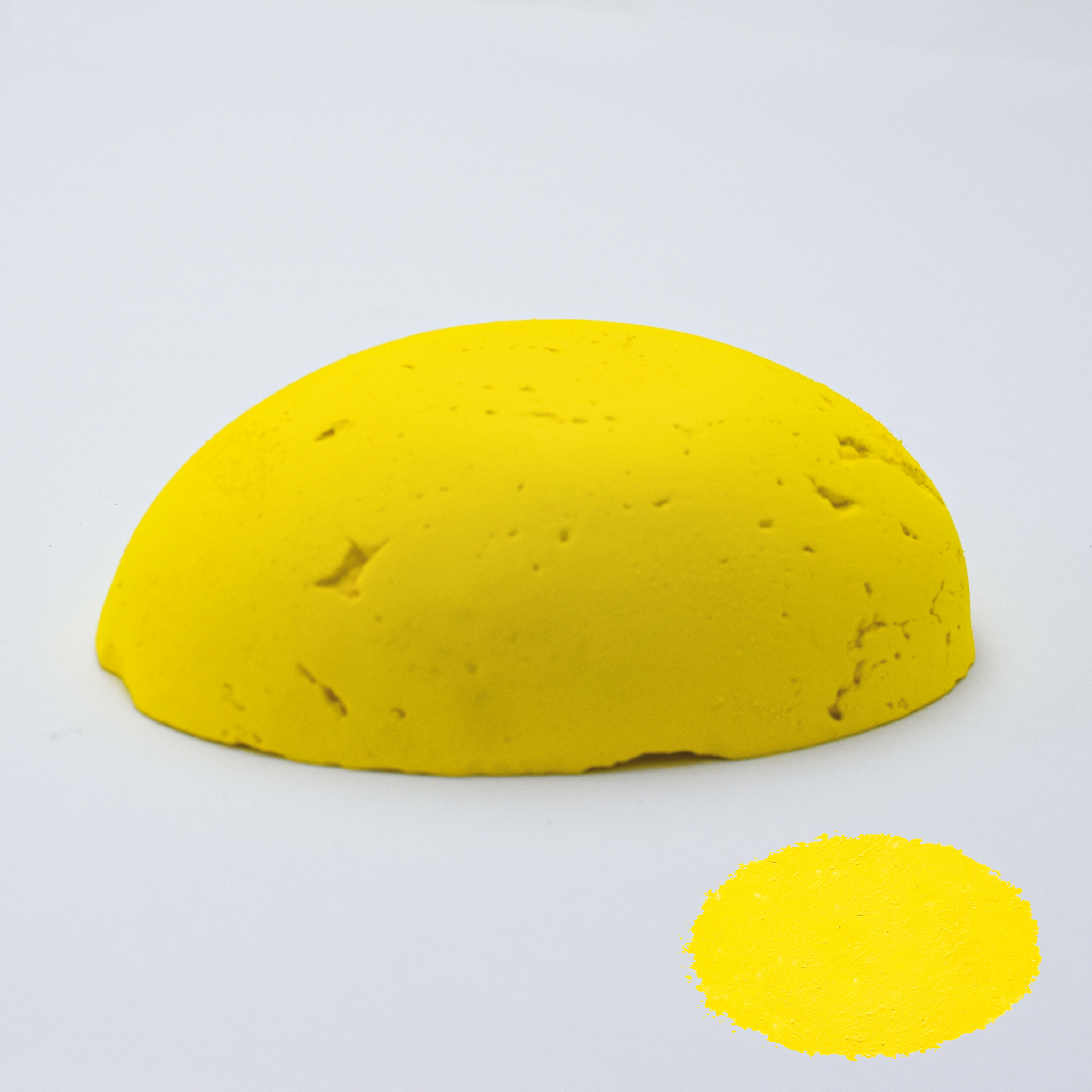 A half egg shaped pastel in a yellow tone, sitting on a white background with a drawn colour swatch.