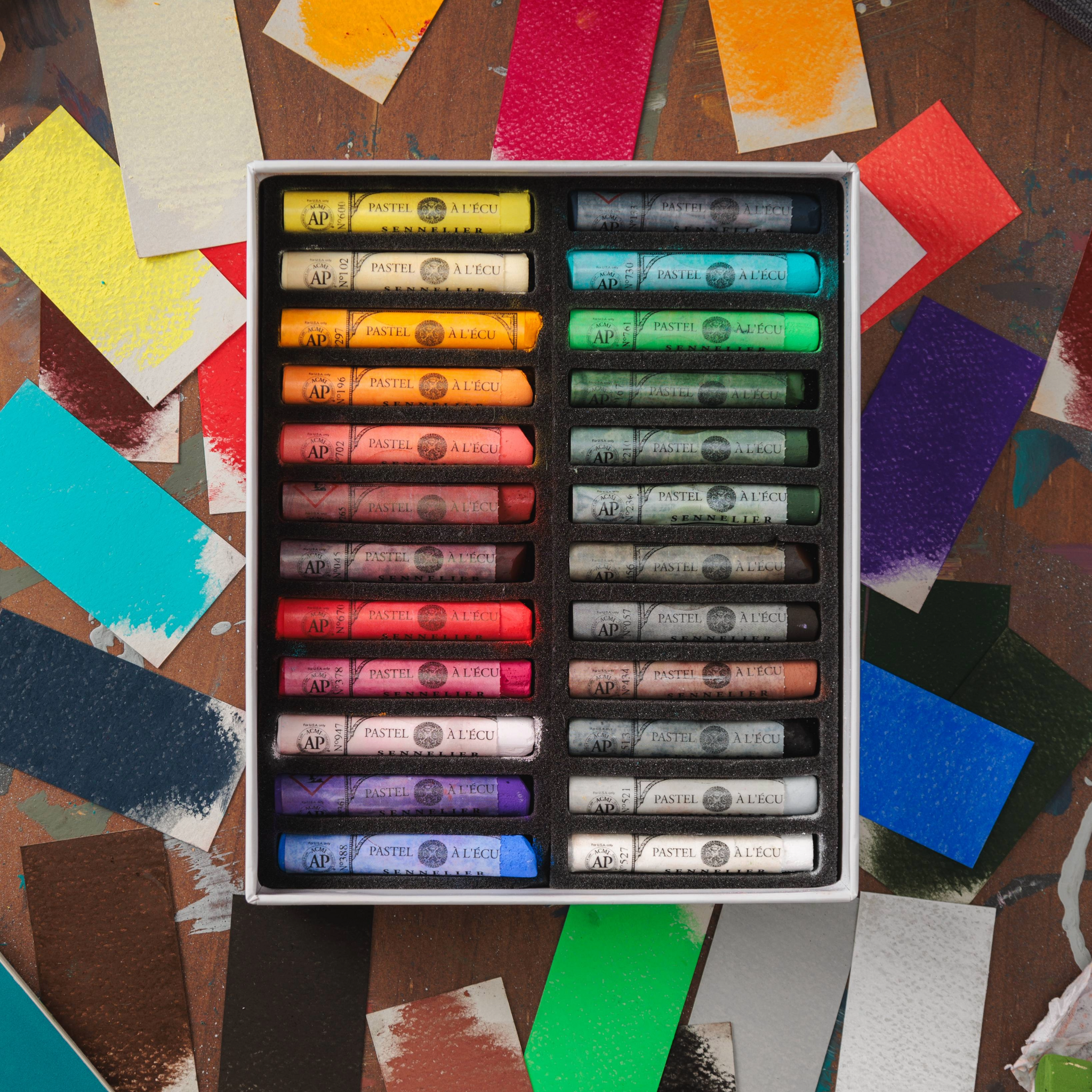 A set of Sennelier extra soft pastels in assorted colours displayed in an open box, with examples of the colour swatches shown beside the box.