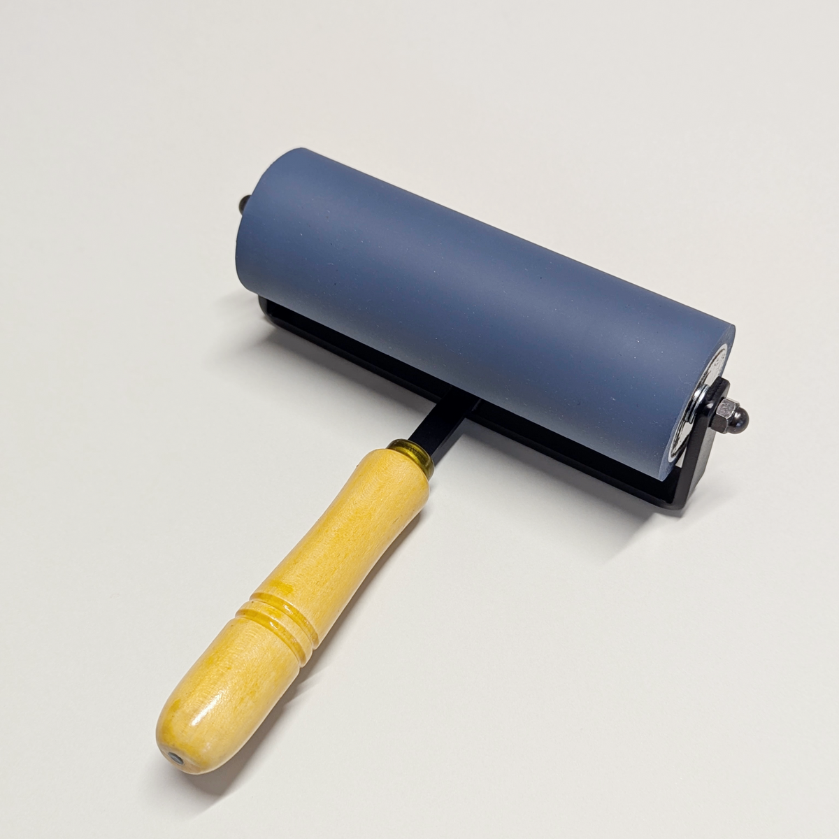 Blue rubber roller with black frame and wooden handle displayed lying down on the bar of the frame on a light grey background