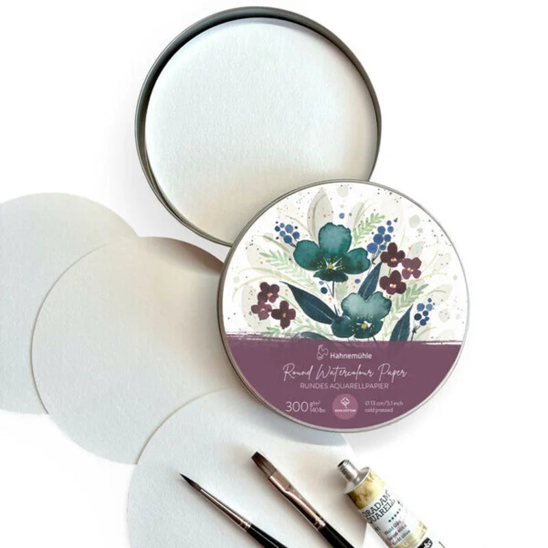 A round tin box with a floral motif on the lid, containing sheets of watercolour paper, displayed alongside two brush and a watercolour paint tube