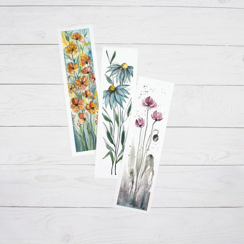 3 bookmark pad papers with floral watercolour designs painted on them. Displayed on a white painted woodbackground.