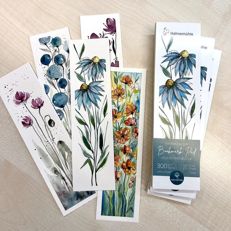 A pile of Hahnemuhle Bookmark pads with a blue floral design on the packaging, displayed next to 5 painted bookmarks in various floral patterns.