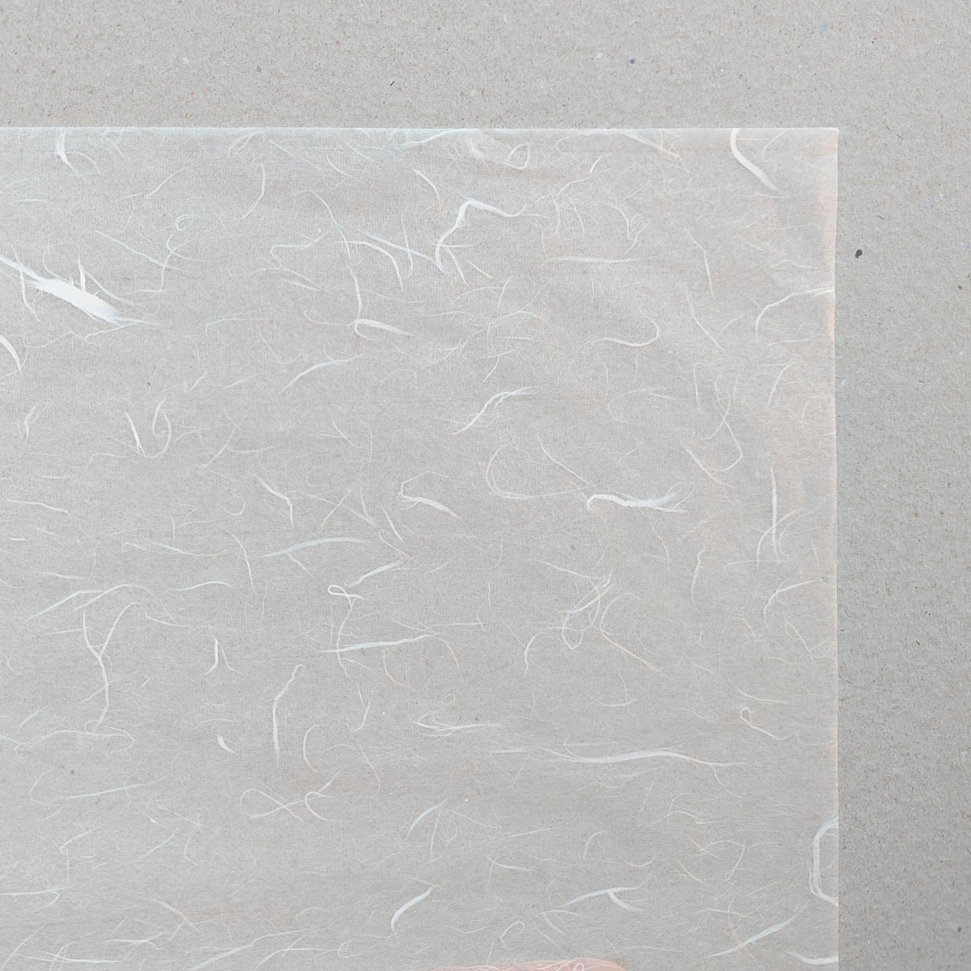 A sheet of Unryu White Light paper with a semi-transparent quality and swirling fibre texture, placed against a grey background.