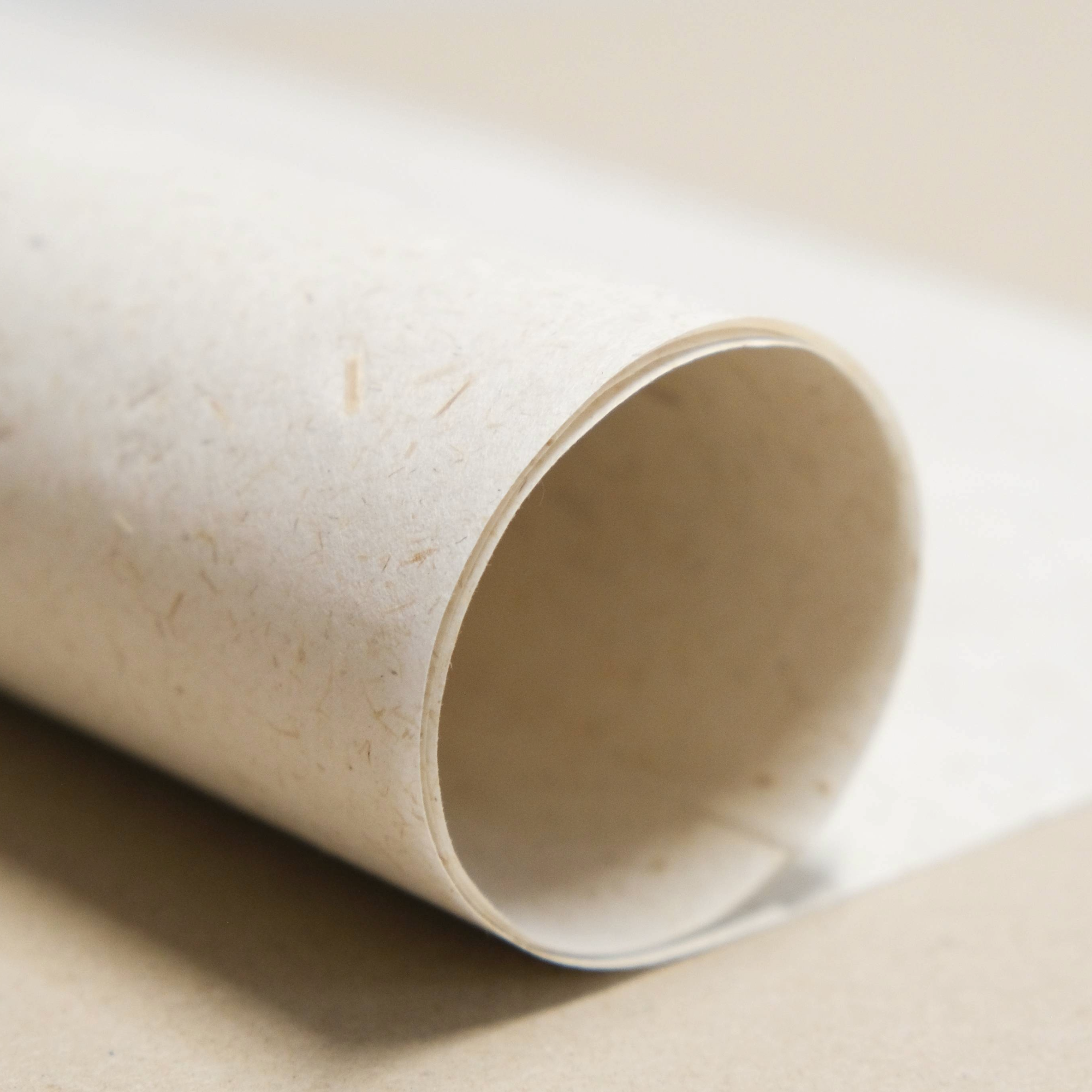 Close-up of a beige fibre flecked paper  rolled up on a brown background.