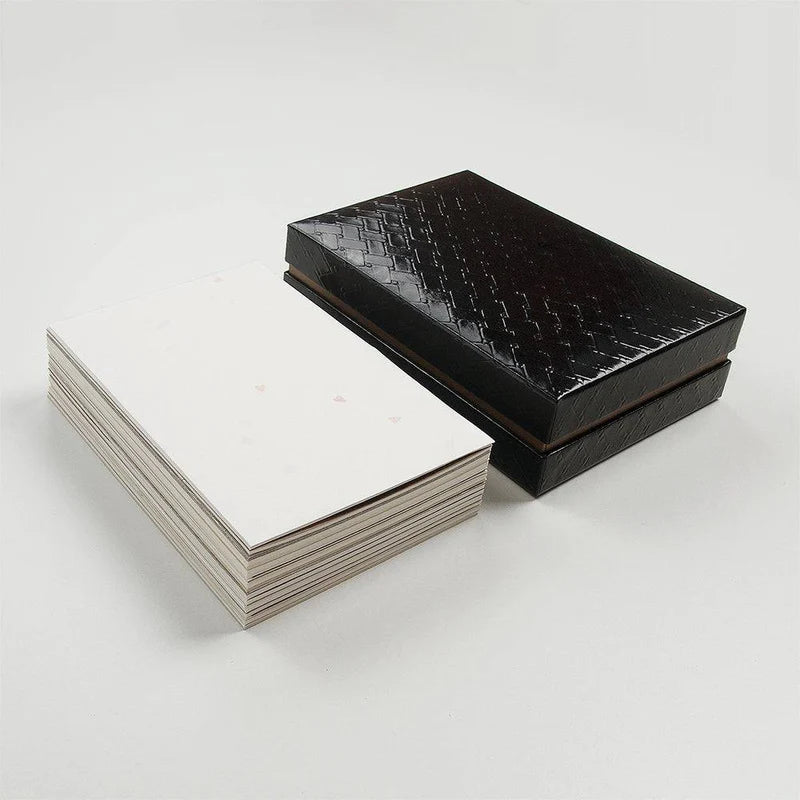 A black lacquered box with a basketweave pattern shown next to a pile of various Japanese papers in neutral tones