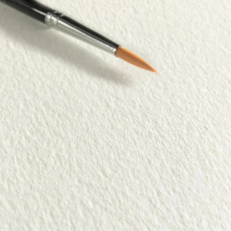 A close up image of a light textured white paper with the top of a black handled brush with a silver ferrule and orange synthetic fibres sitting on top of the paper.