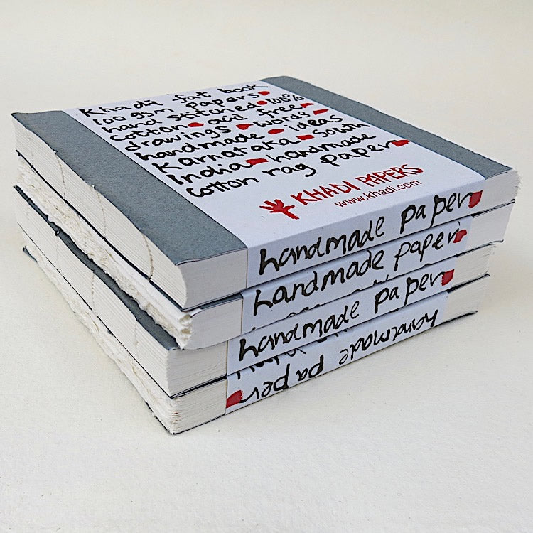 Stack of Khadi Fat Books with dark grey paper covers and packaging with visible text reading 'handmade paper' on the spine, against a white background