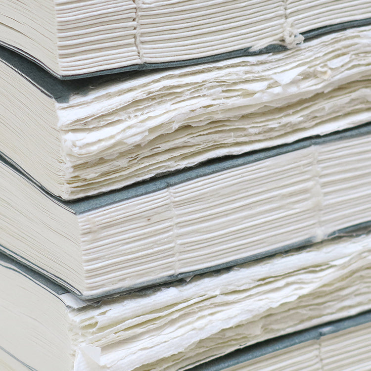 Close up of stacked Khadi fat books showing white paper with grey covers alternating between showing exposed binding and deckled paper edges.