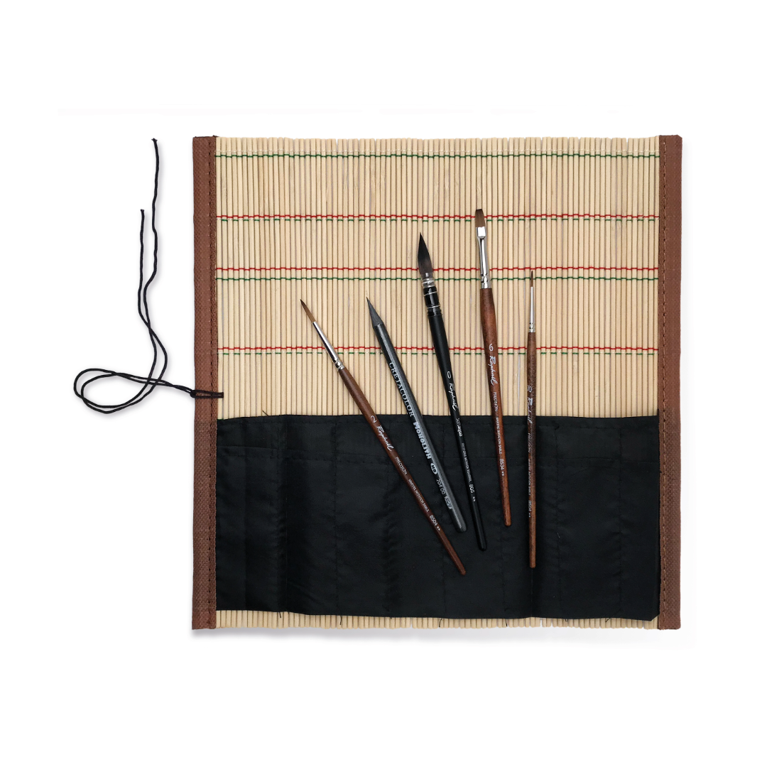 A bamboo brush roll opened out with 4 various paint brushes and a graphite stick splayed ontop.