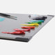 A grey glass slab with corner protectors with a range of coloured oil paints swatched on the top and a brush with blue paint on the end.