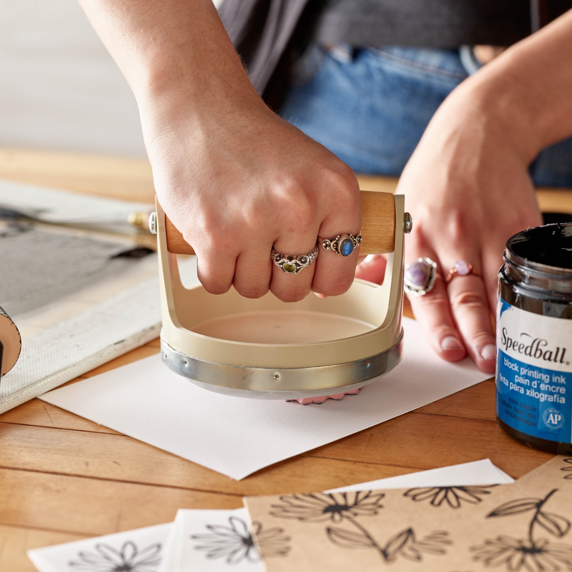 Person using a easy carve block on paper using a speedball teflon baren to hand print.