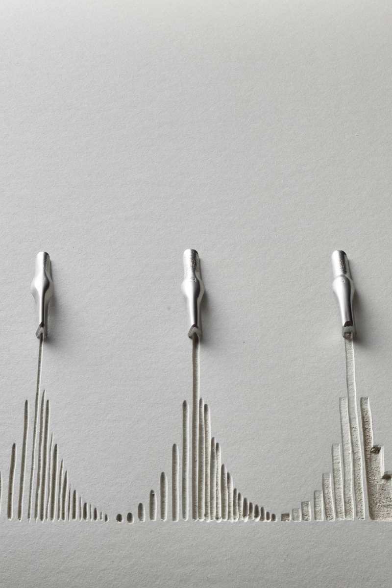 A piece of lino with lines carved out from 5 different cutting tools with each tool head sitting on the lino.