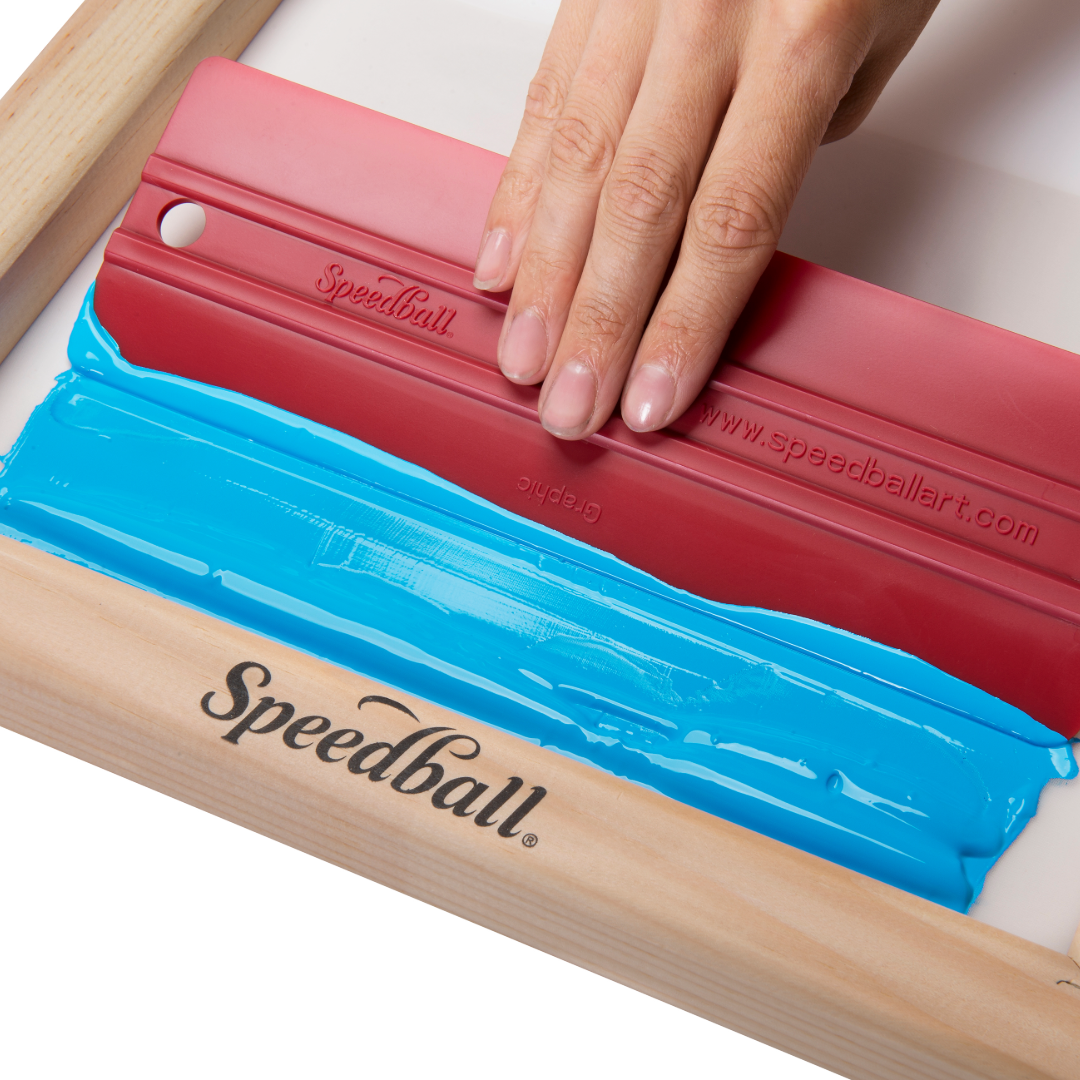 Hand using a Speedball squeegee on a screen printing screen with blue ink.