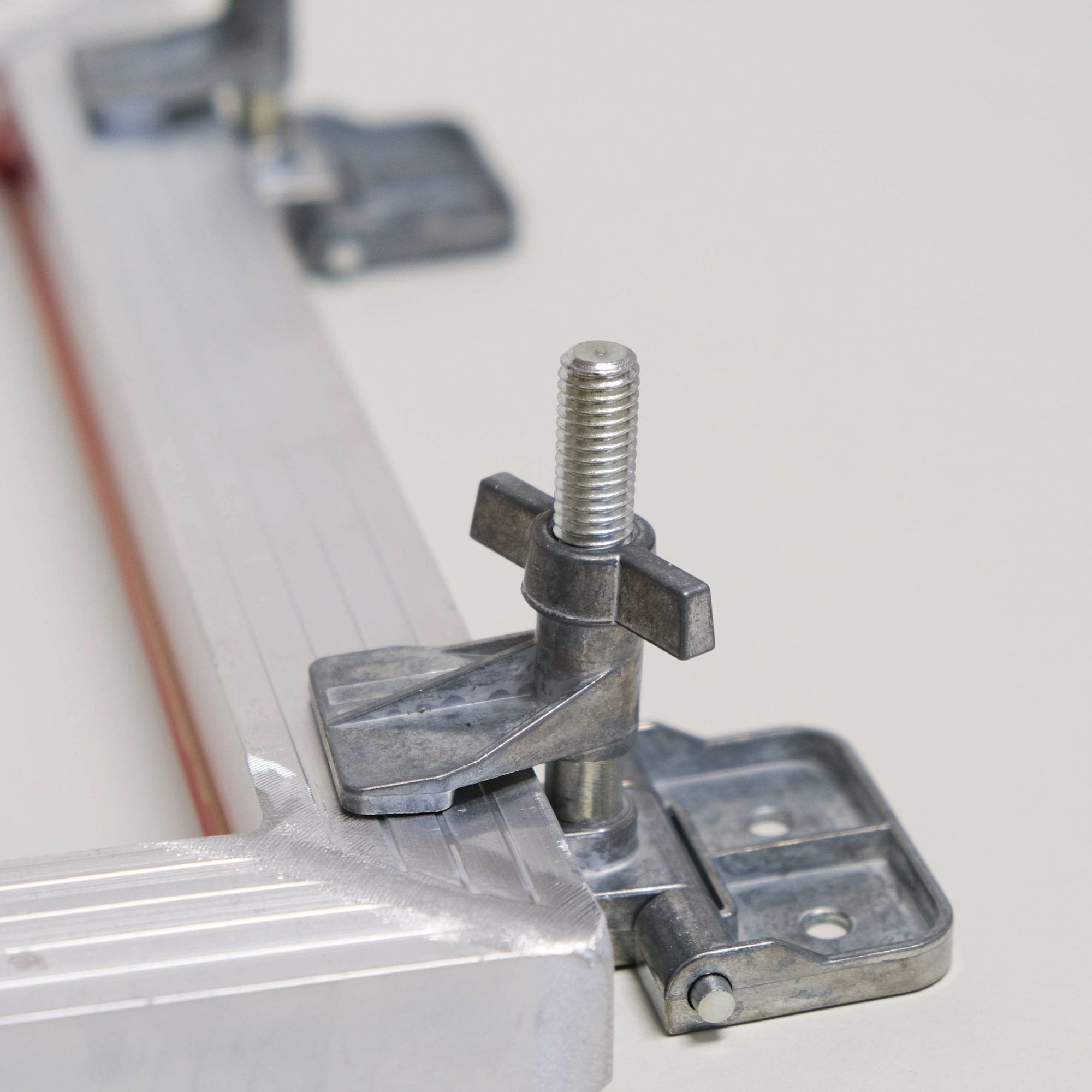 Metal hinge clamps holding the edge of a metal frame on a light surface