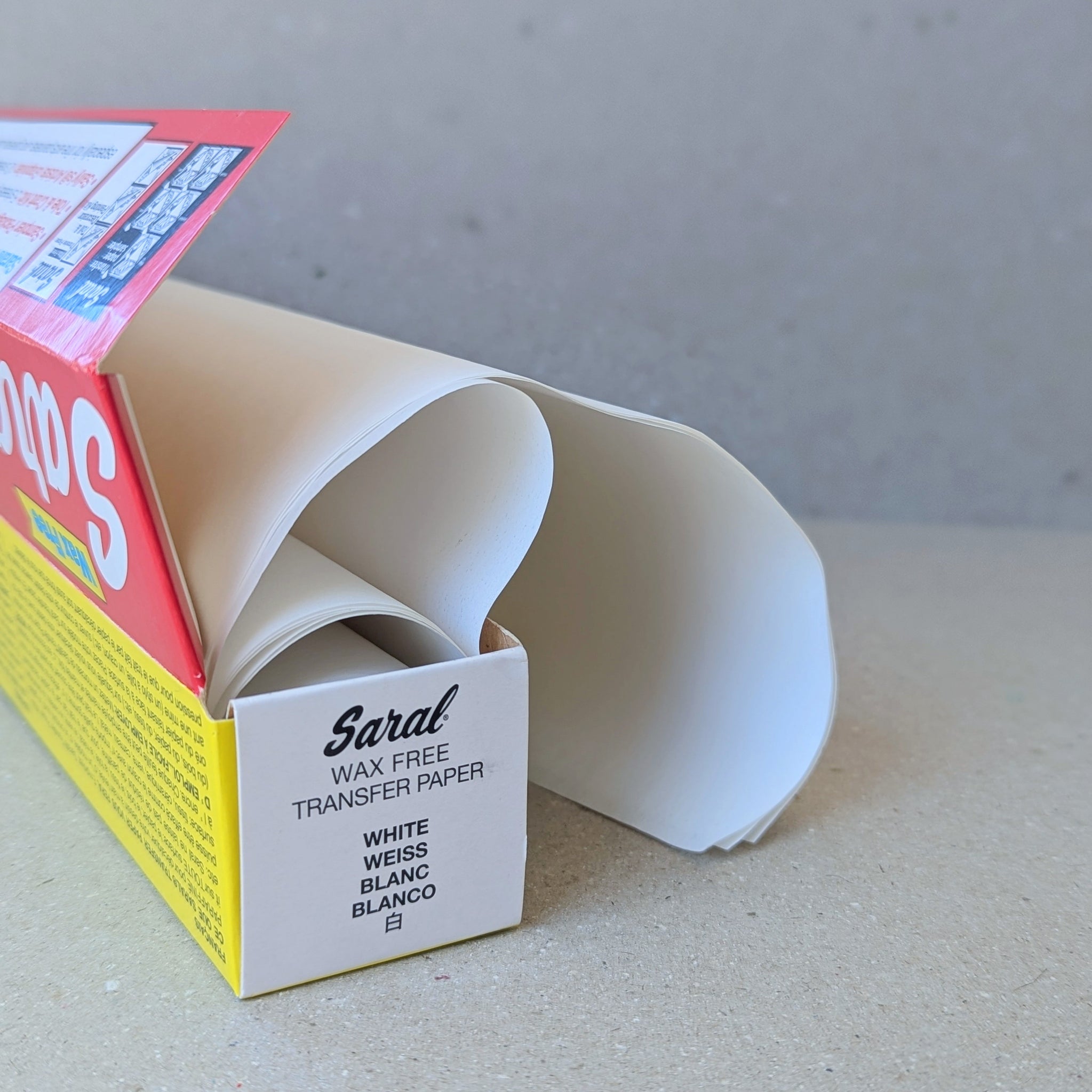 An open box of white Saral Transfer Paper with red and yellow packaging, placed against a beige background.