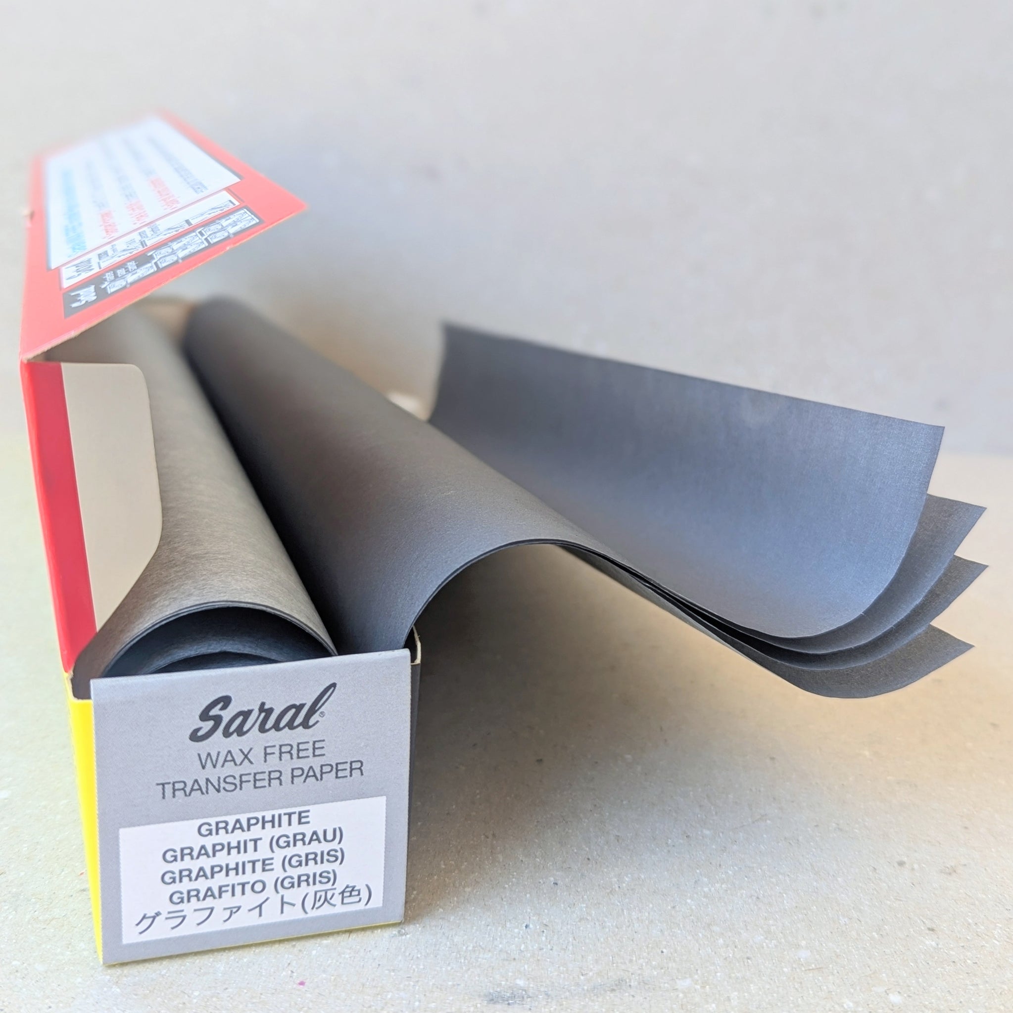 An open box of Graphite coloured Saral Transfer Paper with red and yellow packaging, placed against a beige background.