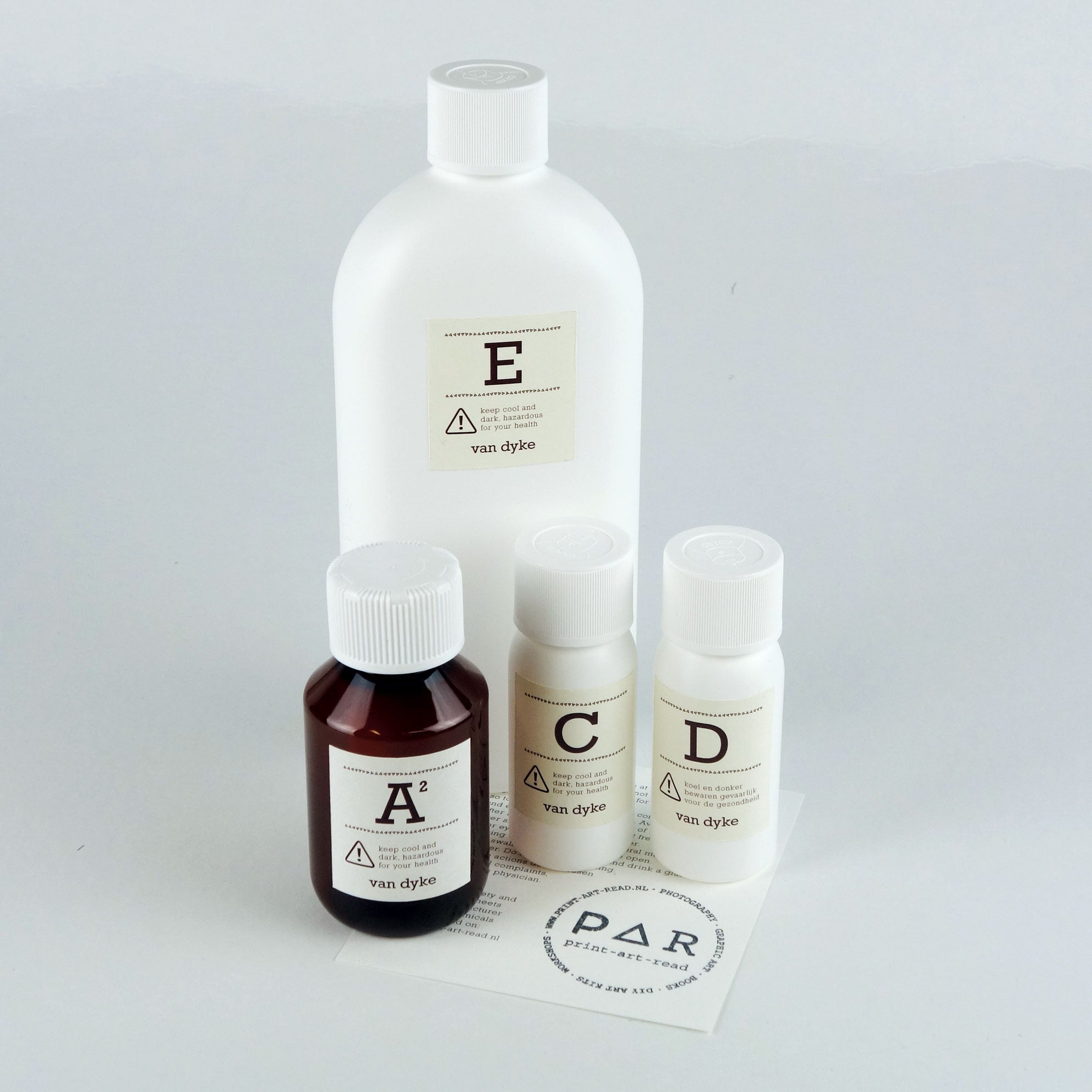 Set of van dyke photgraphic printing chemicals labelled; A,C,D and E of varying size bottles on a light grey background