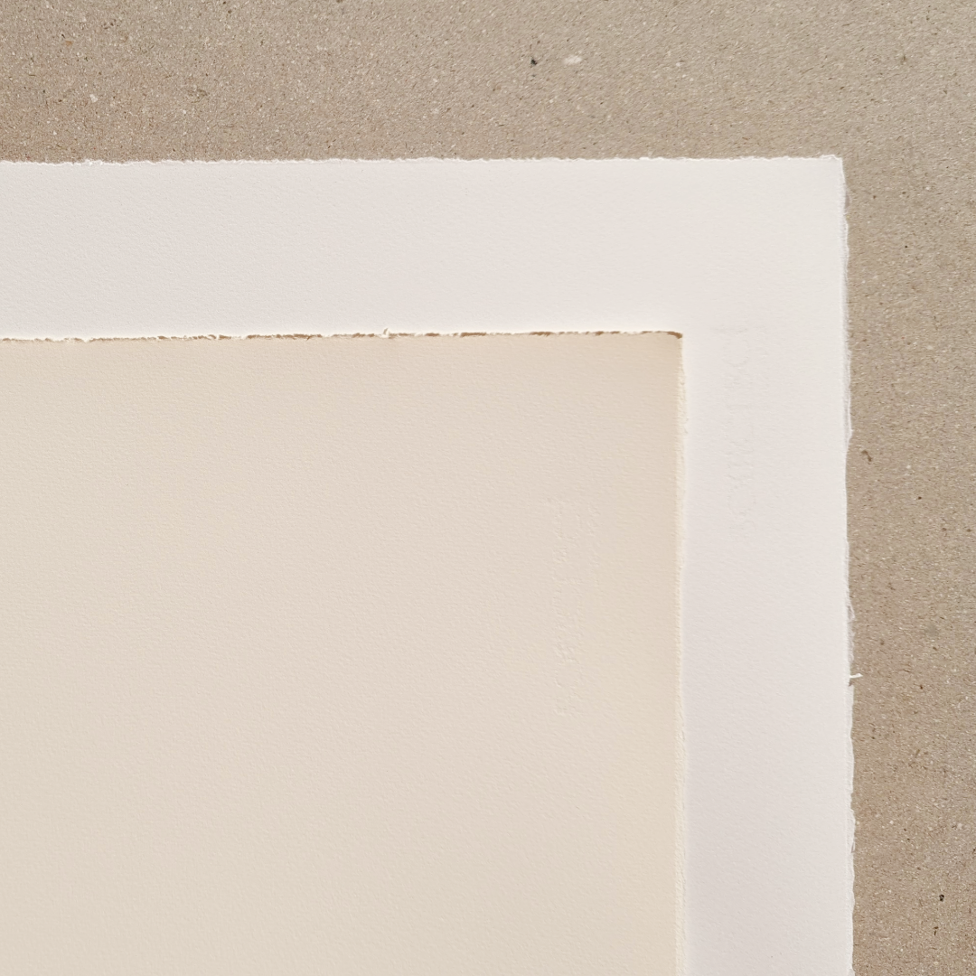 A close-up image of two Somerset Satin papers, once white and one a beige tone. Highlights its smooth, surface and deckled edges against a neutral background.