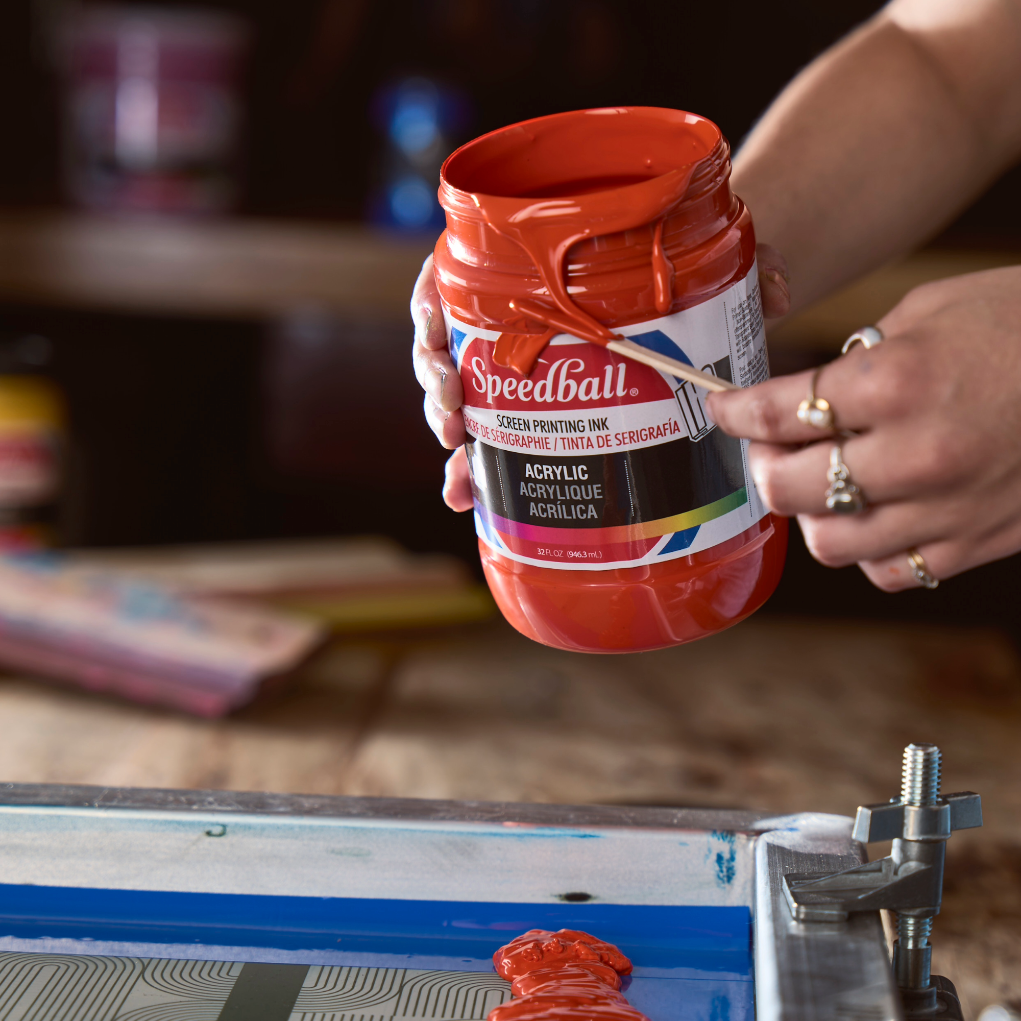 Orange Screen printing Ink open and being poured onto a screen ready to print with studio equipment in the background.