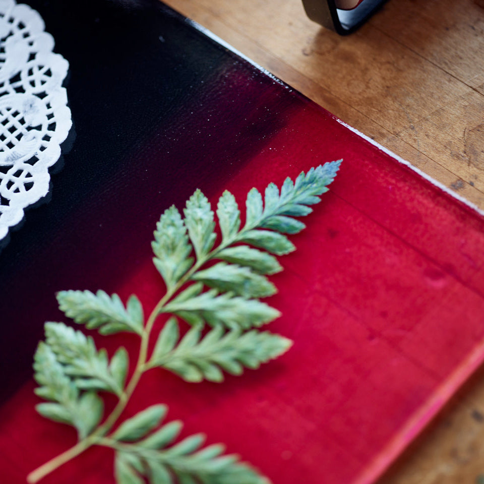 Green leaf and dolly paper on a speedball geli plate that has been rolled up with red and black ink on a wooden table