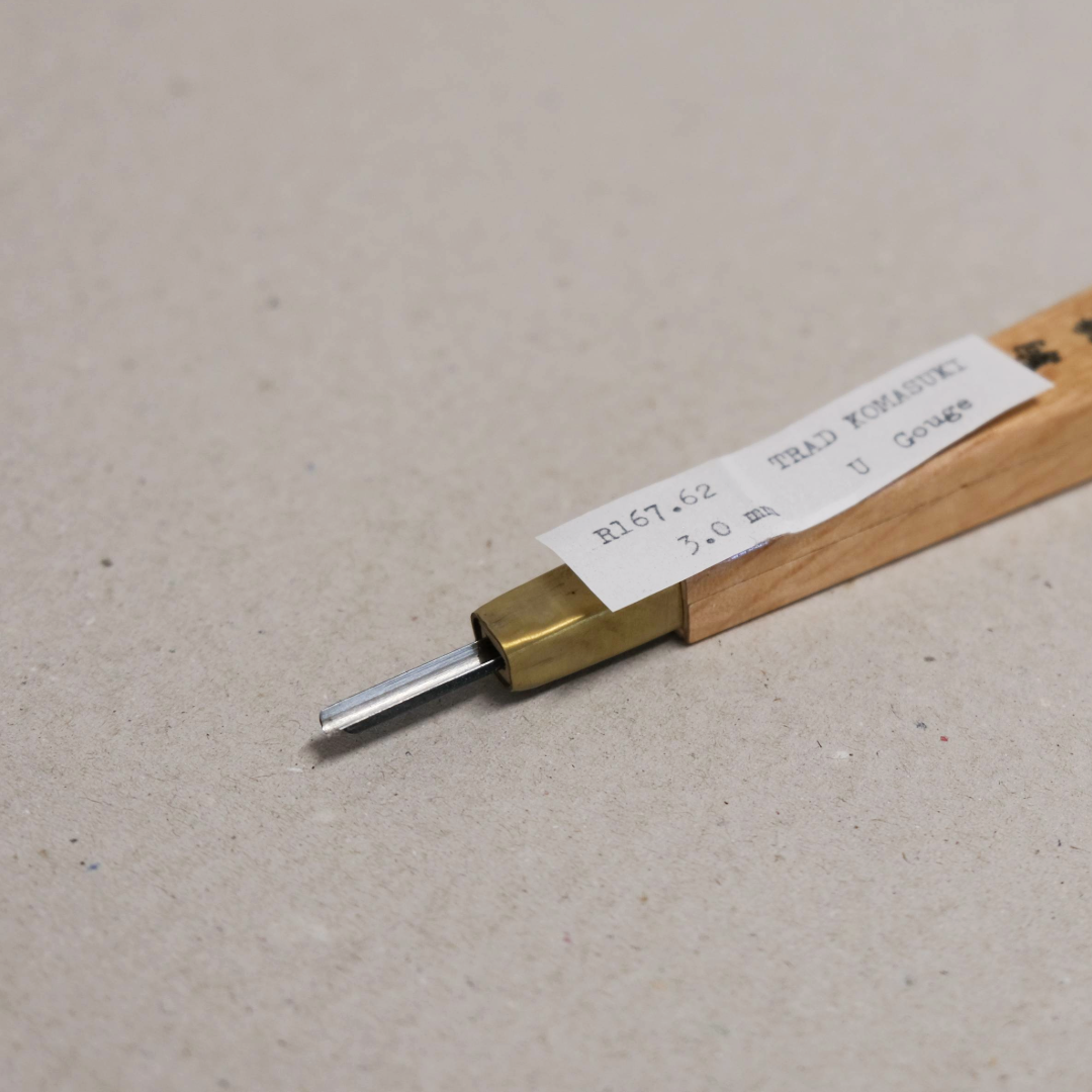 A close-up of a traditional Komasuki 'U' Gouge relief tool with a wooden handle, brass ferrule and a steel blade.