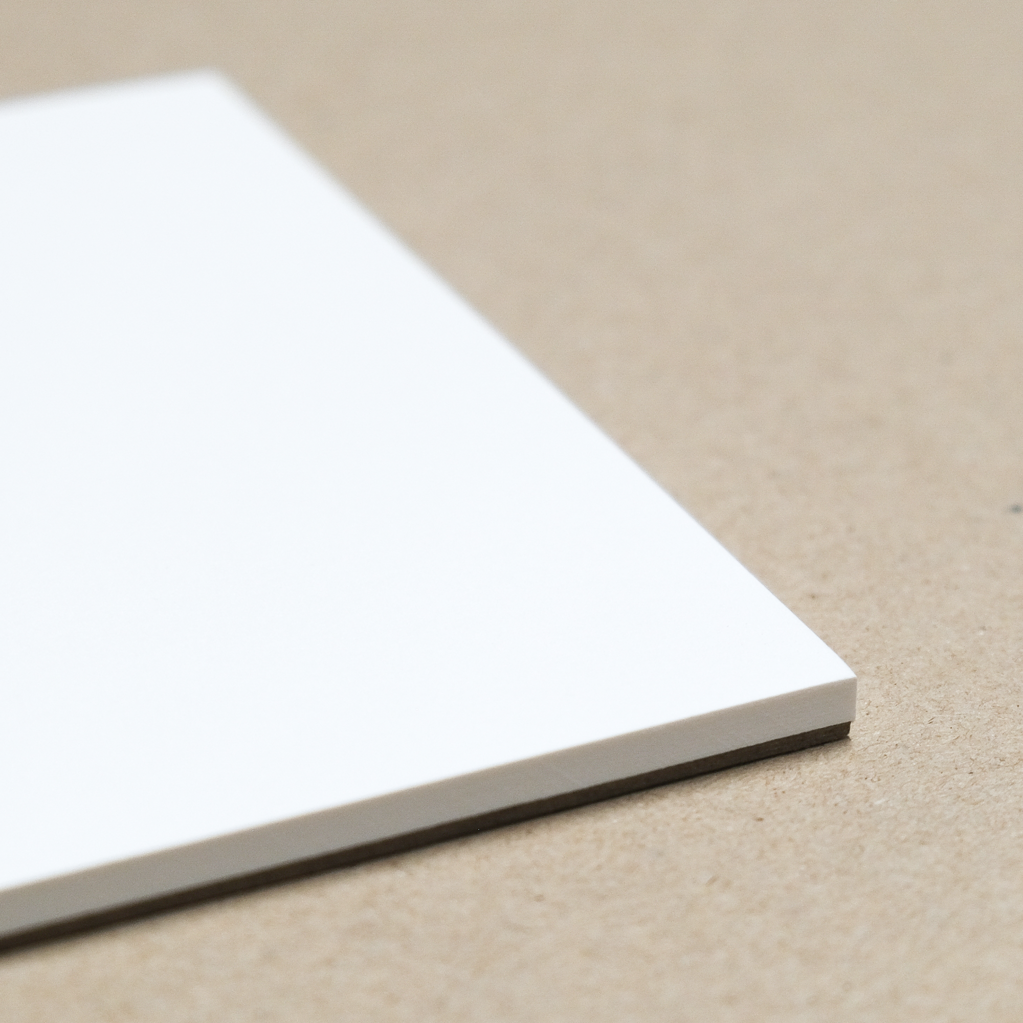Close up of a corner of a paper pad showing smooth white paper stacked on a cardboard backing. Shown against a light brown background.