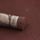 A close-up of a brown Sennelier extra soft pastel with the colour information printed on the paper wrap.
