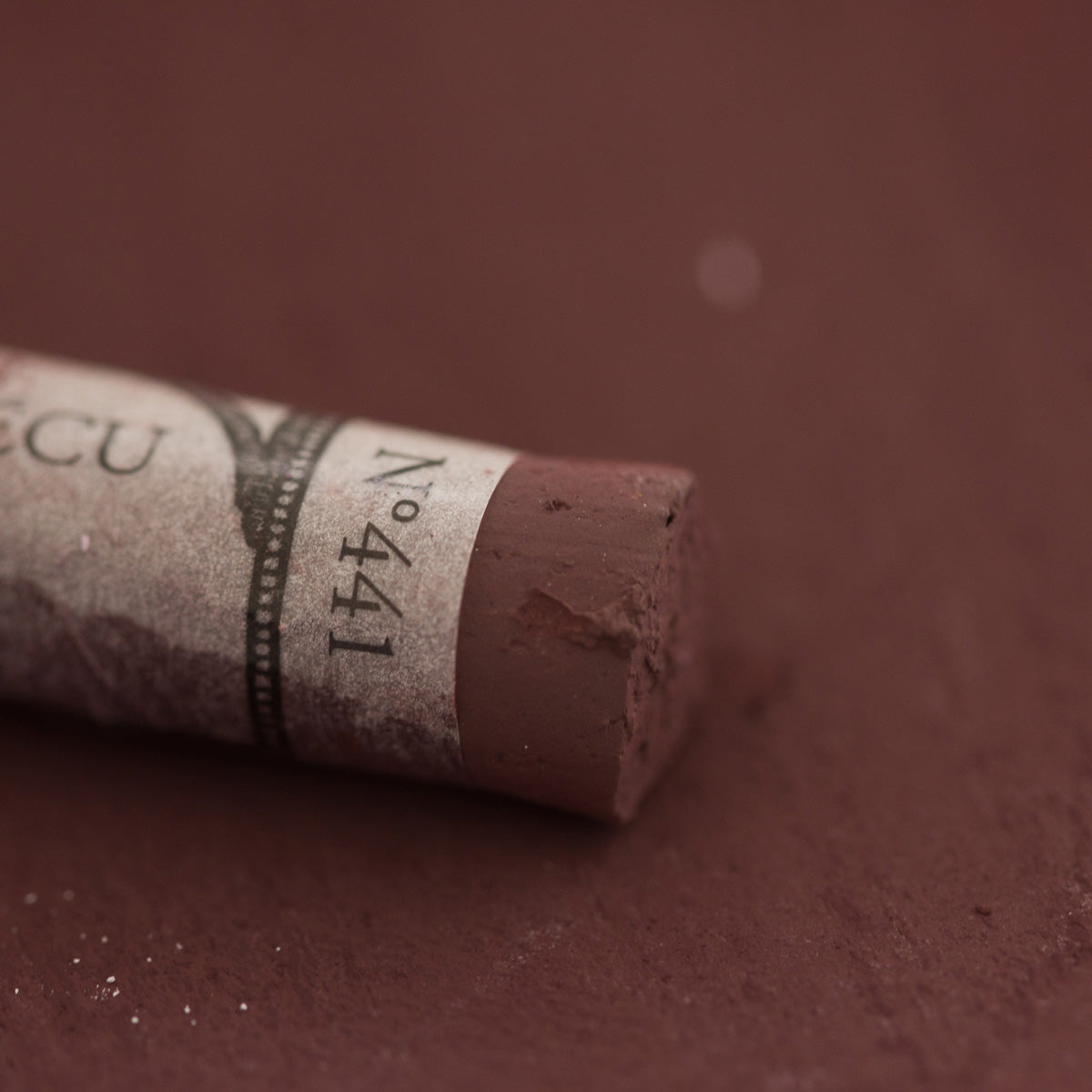 A close-up of a brown Sennelier extra soft pastel with the colour information printed on the paper wrap.