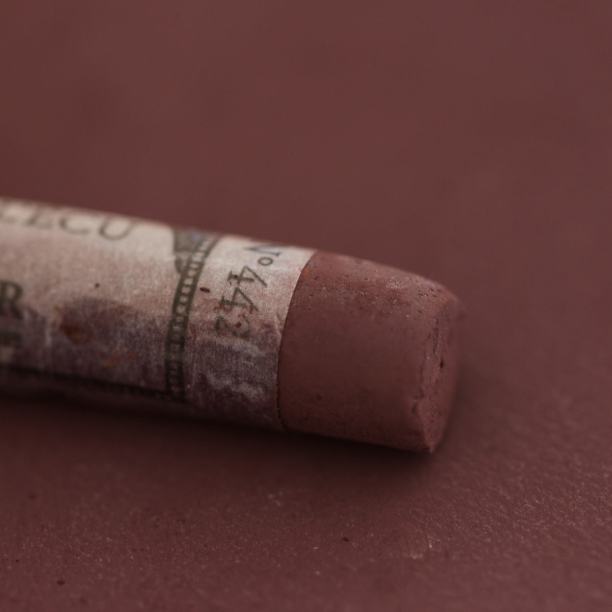 A close-up of a brown Sennelier extra soft pastel with the colour information printed on the paper wrap.